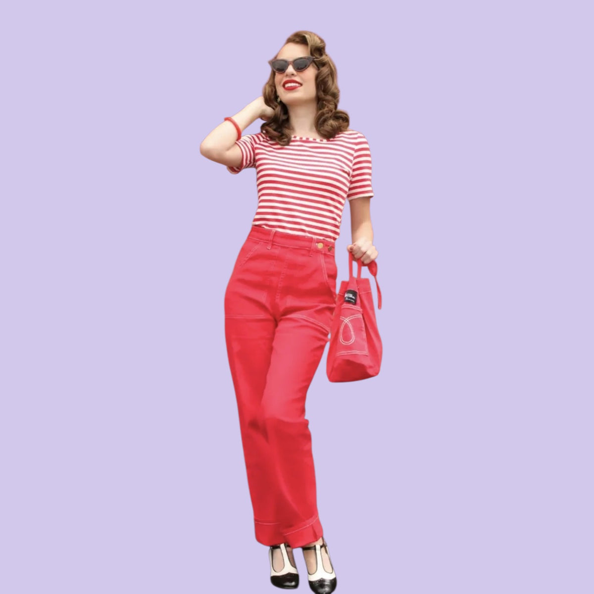 A woman modeling a red and white striped short-sleeve top, bright red pants, black and white heels, sunglasses, and a red handbag against a solid light purple background.